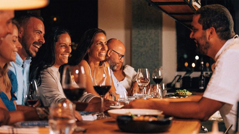 Excited patrons sit at at a bar top with glasses of wine