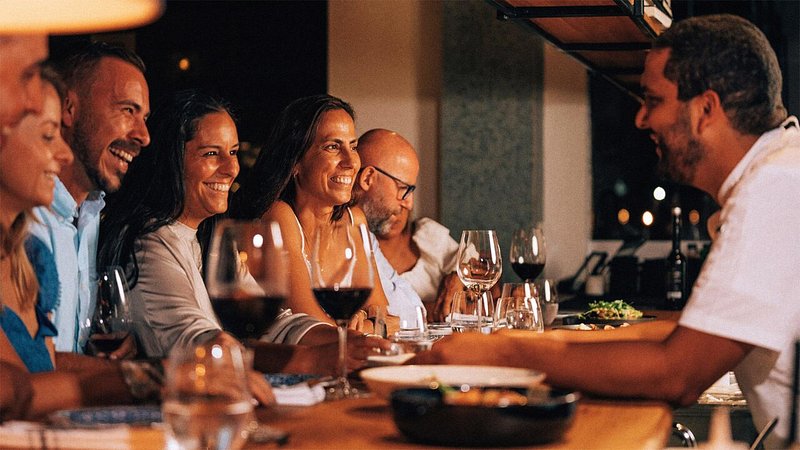 Excited patrons sit at at a bar top with glasses of wine