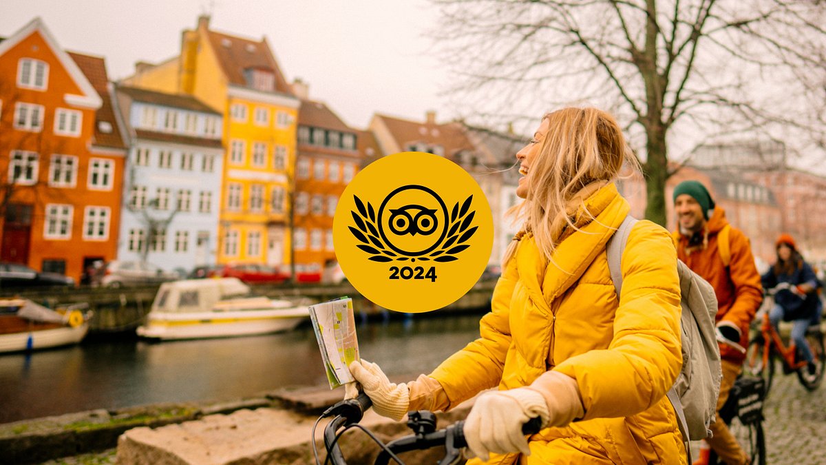 Um grupo de viajantes a andar de bicicleta na colorida zona ribeirinha de Nyhavn em Copenhaga, na Dinamarca, com um logótipo dourado dos Prémios Travellers' Choice - O melhor dos melhores