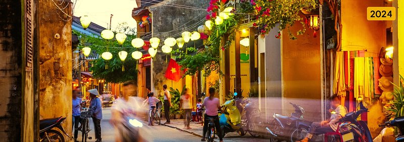 Habitantes locais a explorar a Cidade Antiga de Hoi An, no Vietname, iluminados por lanternas suspensas