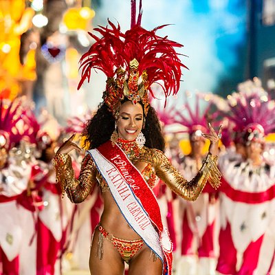 Μια γυναίκα με αξεσουάρ στο κεφάλι και στολή σε έντονο κόκκινο χρώμα βρίσκεται μπροστά σε μια πομπή καρναβαλιού στο Ρίο ντε Τζανέιρο