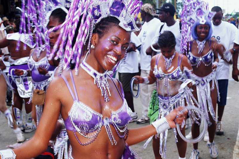 Μια νεαρή κοπέλα με μοβ κοστούμι σε στιλ μπικίνι, χορεύει μαζί με άλλους χορευτές στο καρναβάλι του Τρινιντάντ