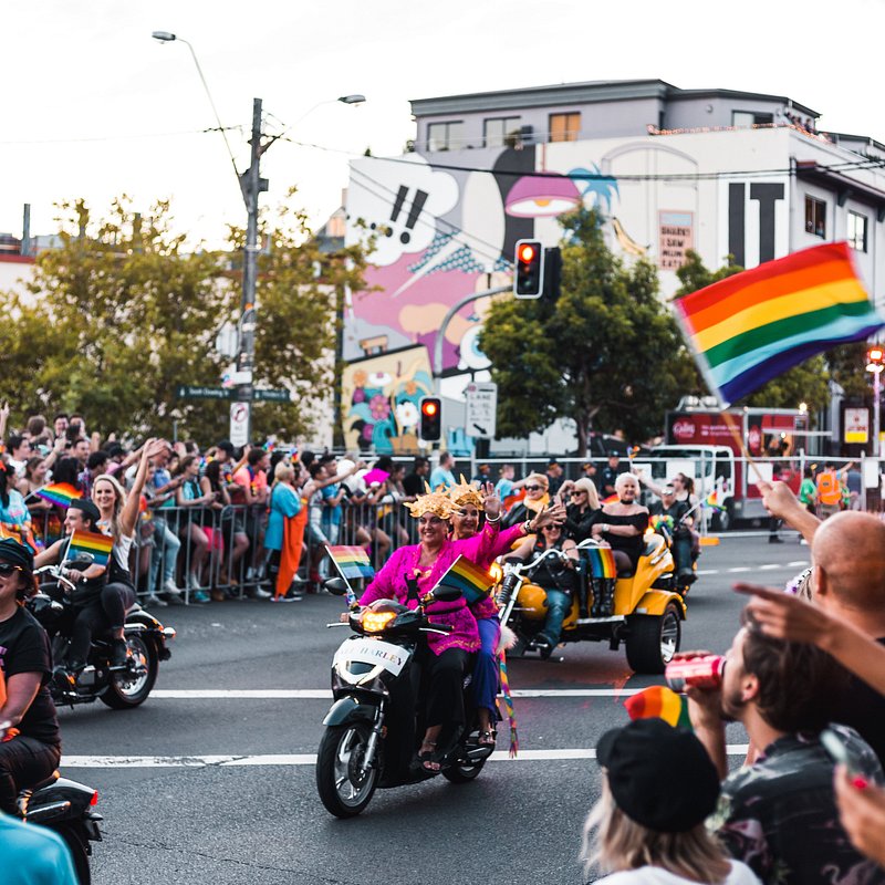 시드니 게이 및 레즈비언 마디 그라 퍼레이드에서 사람들이 오토바이를 타고 지나갈 때 무지개 깃발을 흔들고 있는 많은 군중