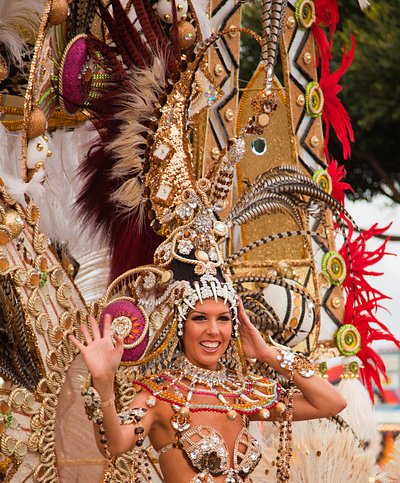 Μια γυναίκα με ένα τεράστιο και περίτεχνο αξεσουάρ στο κεφάλι χαιρετάει το πλήθος στο καρναβάλι της Σάντα Κρουζ της Τενερίφης