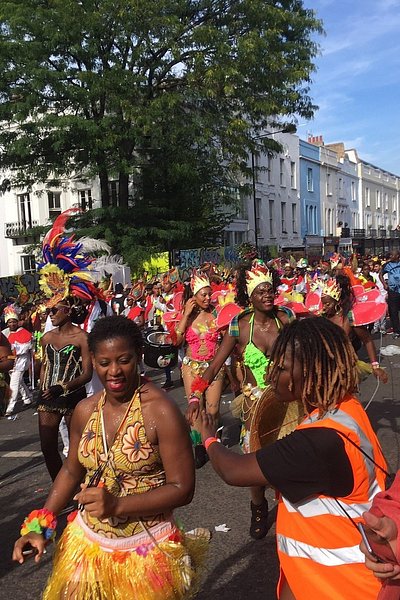 Γυναίκες φορούν πολύχρωμες στολές με φτερά και παρελαύνουν στον δρόμο στο καρναβάλι του Νότινγκ Χιλ