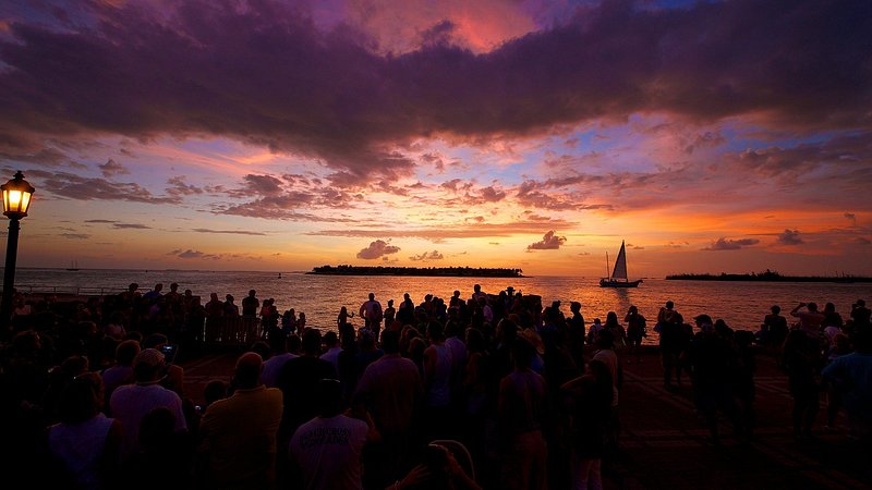 A sailboat on the horizon of a pink-purple sunset in the last light of the day at Mallory Square