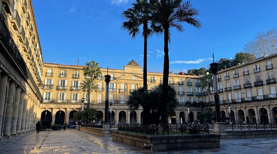 Plaza Nueva in Bilbao's Casco Viejo, a grand neoclassical square with arcaded buildings and people enjoying outdoor cafes.