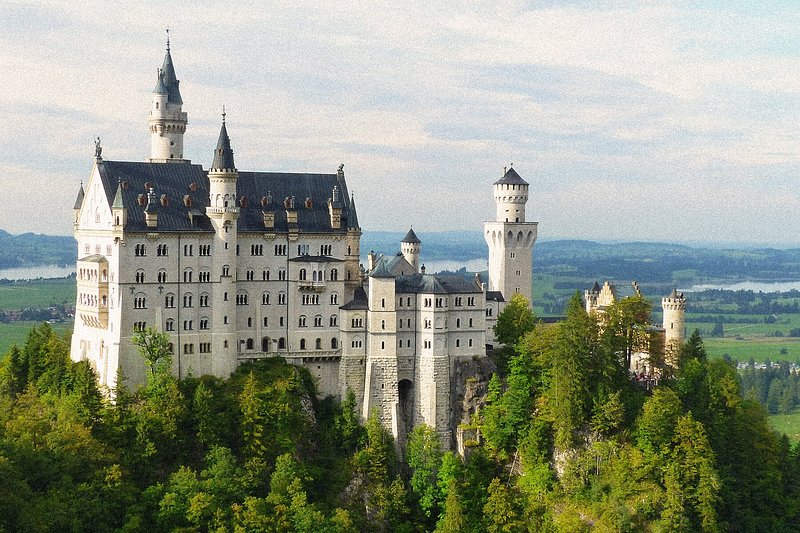 An aerial view of the Neuschwanstein Castle in Germany atop a hill surrounded by greenery