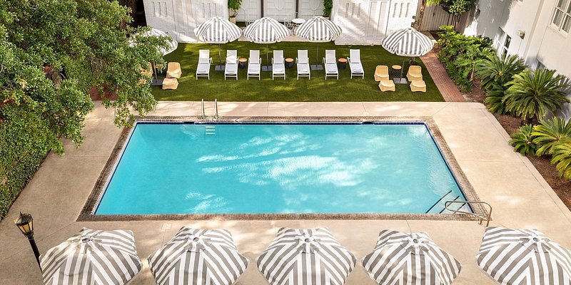 Aerial view of outdoor pool lined by loungers and striped umbrellas set in garden