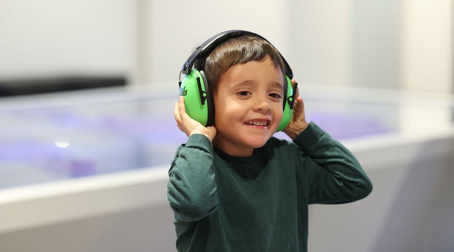 A photograph of a child wearing ear defenders and smiling.