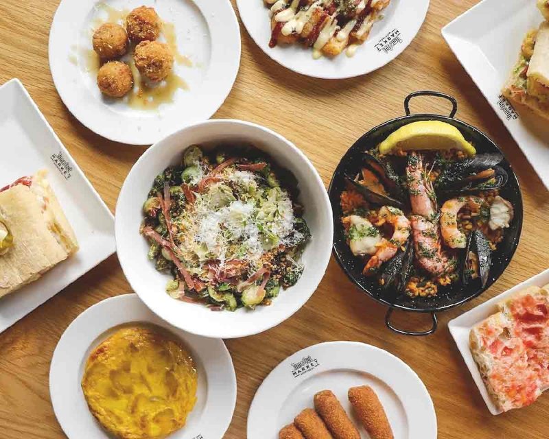 Wooden table topped with various dishes such as Brussels sprouts, seafood, and sandwiches