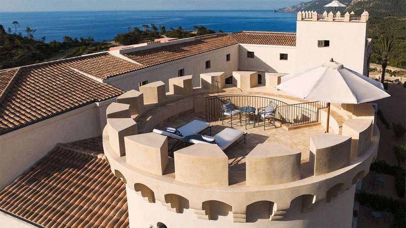 The top of a tower furnished with two loungers and a white umbrella. 