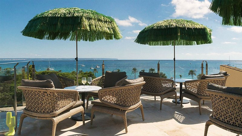 Green raffa umbrellas and patio dining sets by a waterfront view.