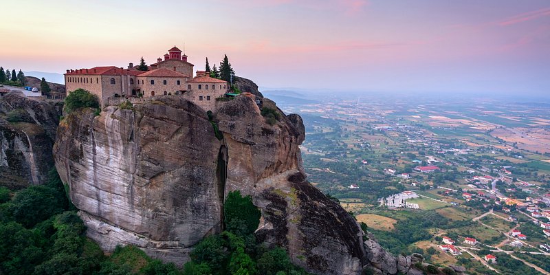 View of Meteora Monastery sitting high atop rock at sunset