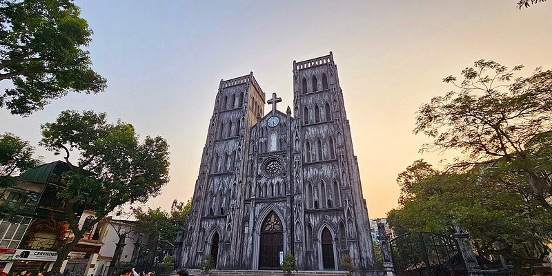 Exterior of tall gray cathedral with cross at the top-center