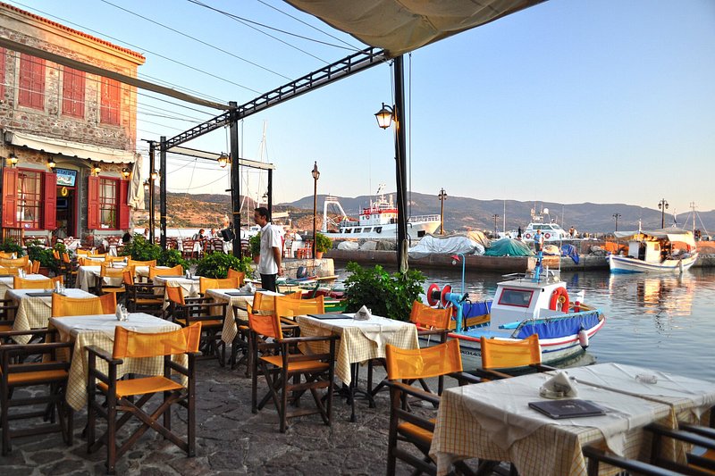 Medieval village Molivos is in the north of Lesvos island, Greece. View of the harbor with fish restaurant on the coast and waiter is ready for the customers.