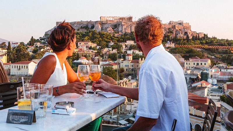 Couple drinking in front of the Acropolis at sunset, in Athens, Greece