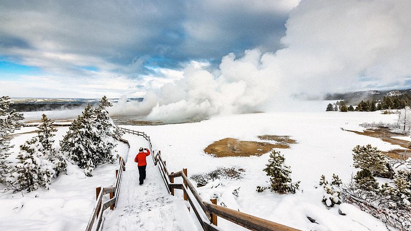 Hiker walking up to geyser in Yellowstone, in the winter