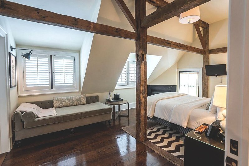 Modern, neutral-tone guest room with exposed wood beams, gray couch, and zigzag rug