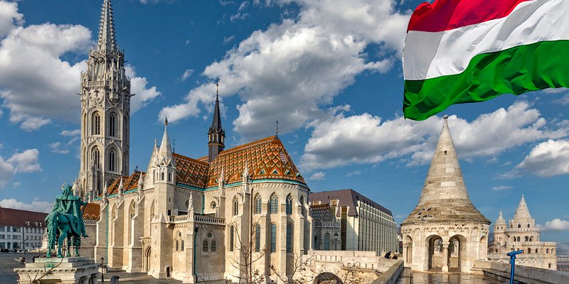 The Matthias Church with its roof decorated with colourful tiles with the equestrian statue of King Stephen I seen from The Fisherman's Bastion and waving Hungarian flag in Budapest