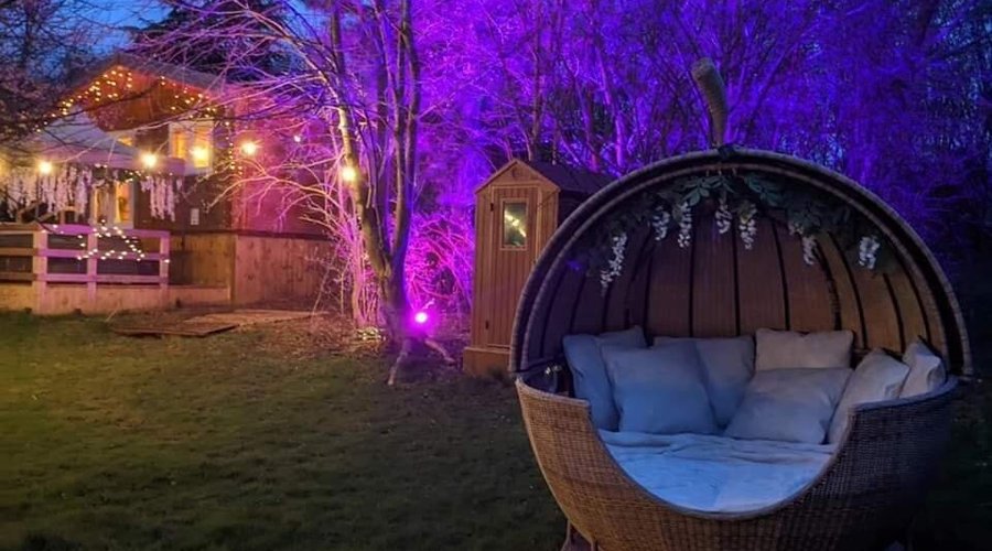 Swan Lodge sounds like a dreamy haven for a romantic escape. Envision this: as the sun dips below the horizon, the lodge transforms into a magical scene, beautifully illuminated by soft, ambient lights. The tranquil atmosphere envelops you as you step outside onto the large garden area, where lush greenery surrounds you, creating a sense of seclusion and intimacy. In the heart of the garden, you discover a cozy day bed for two, elegantly positioned to capture the last rays of sunlight. 