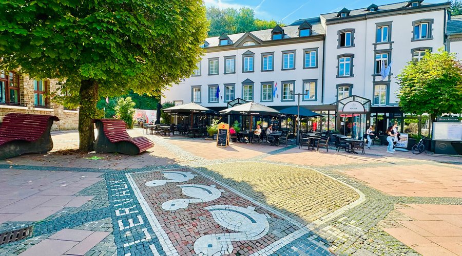Photo de la façade extérieur de l'hôtel avec terrasse ensoleillée sur la plaçette du piétonnier de Clervaux.