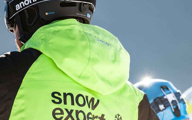 Ein Snow Experts Skilehrer, von hinten zu sehen, gibt einem SkischülerTipps im Skigebiet KitzSki.