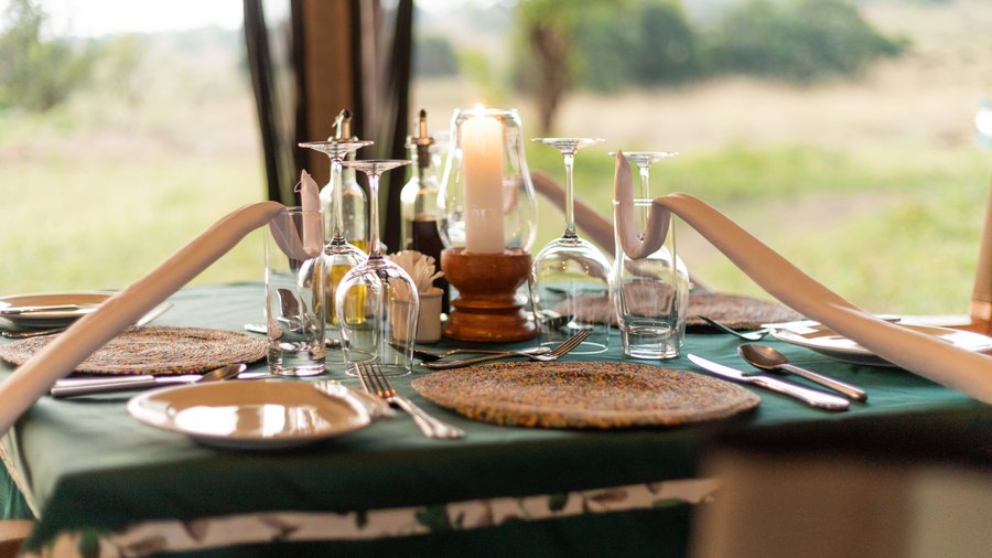 A beautifully set table with sparkling clean glassware and a softly glowing candle, creating an inviting and elegant atmosphere for a memorable dining experience at Untamed Migration Camps.
