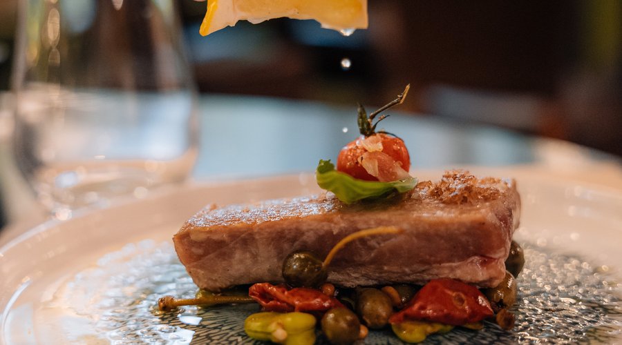 Retour de pêche selon arrivage sur lit de fleurs de câpres, olives Taggiasche, pignons de pin, tomates cerises, fèves, zestes de citron vert et jaune.