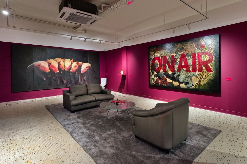 Exhibition room with enormous paintings and seating.