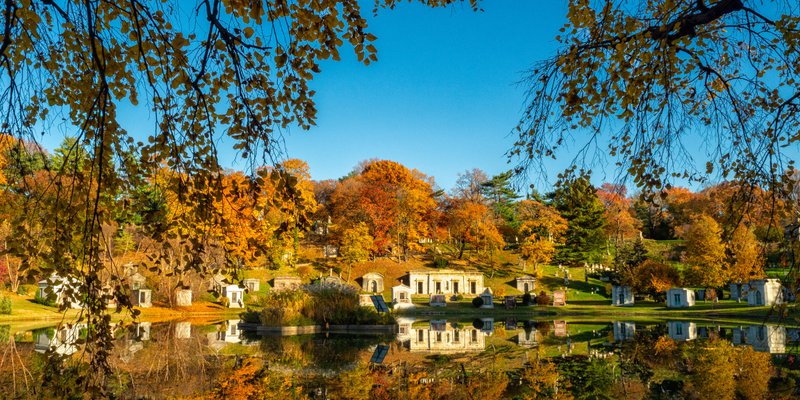 View of autumn trees and tombstones lining lake in cemetery