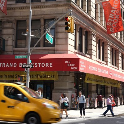 Exterior of corner bookstore, with people walking on sidewalks and a taxi going by