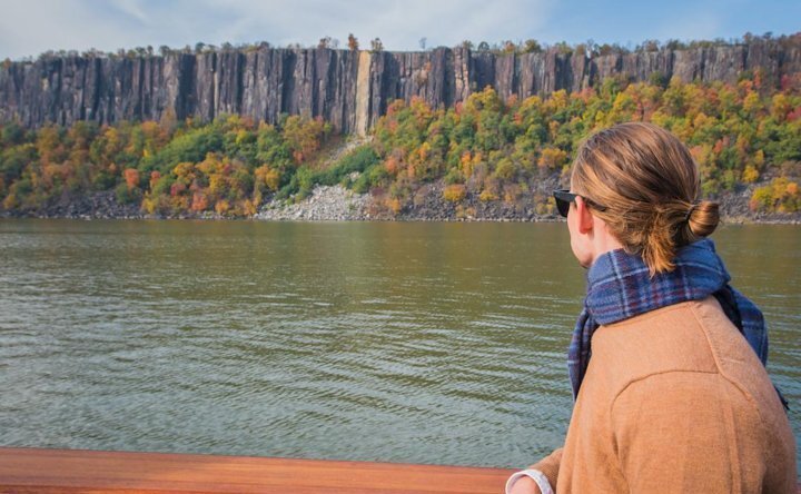 Back of head of someone on river cruise looking out toward autumn tree-lined shoreline