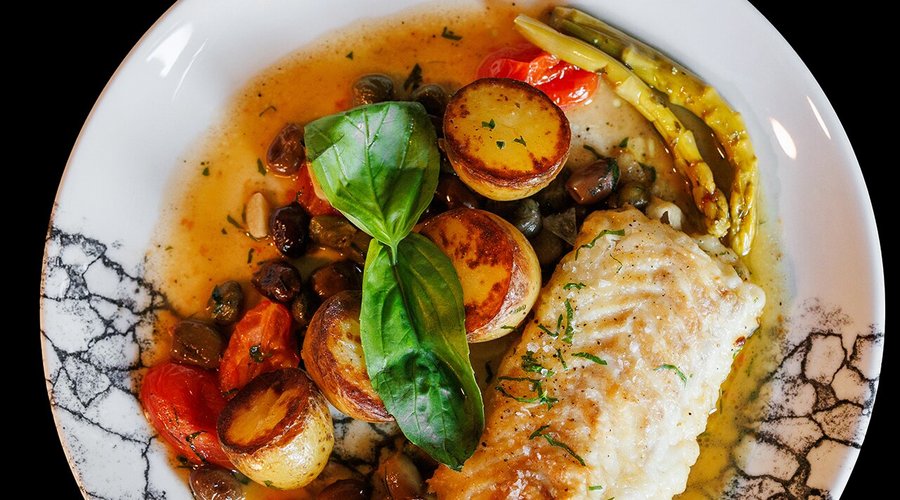 Pan-fried Mediterranean Cod fillet with potatoes, cherry tomatoes, Taggiasca olives, garlic, capers, herbs, and marinated asparagus.