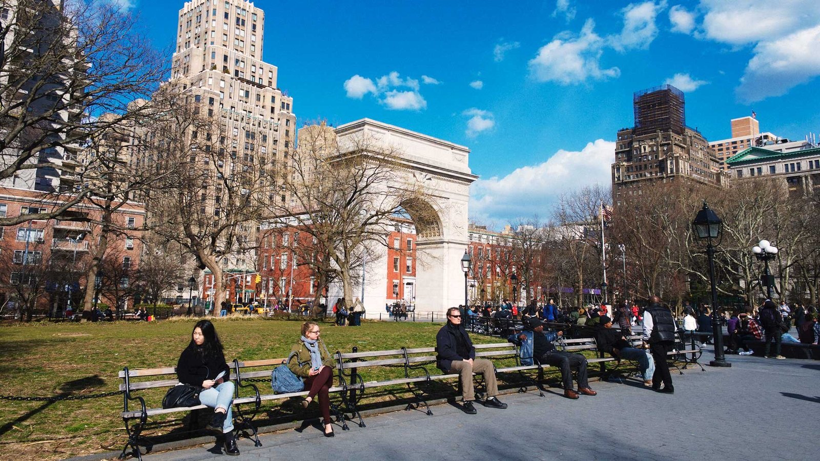 Personas relajándose bajo el sol en bancos del Washington Square Park